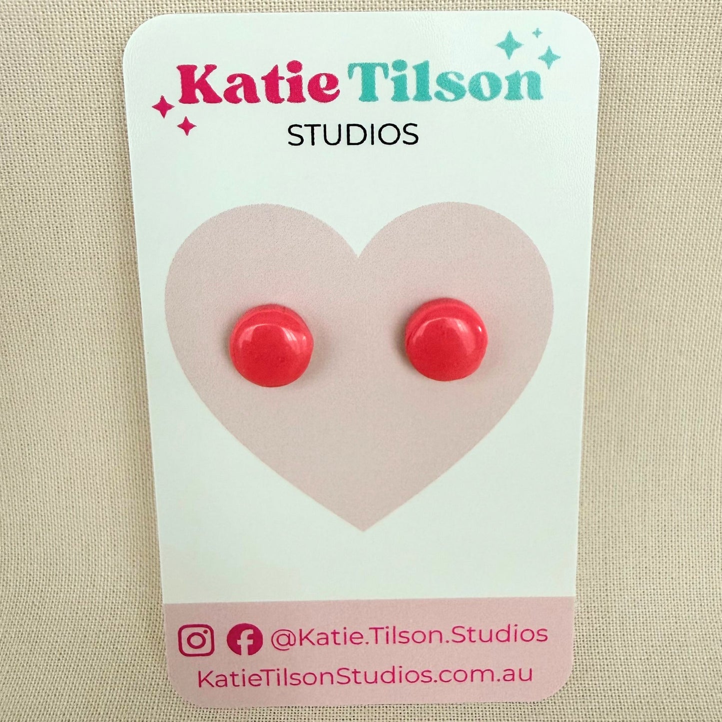 Pink circular stud earrings on a Katie Tilson Studios card against a beige background.