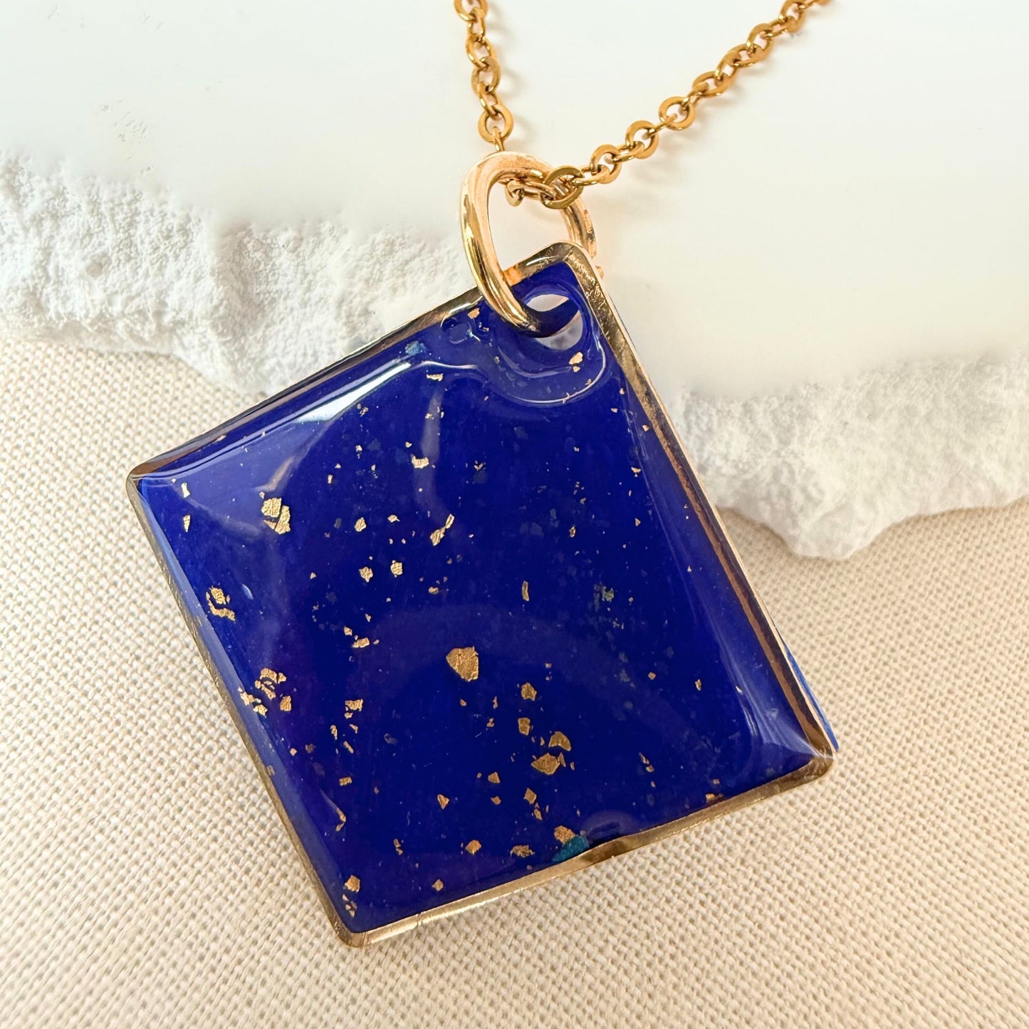 Shine On cobalt colour handmade pendant necklace in diamond shape with gold leaf detail and glossy finish hanging from gold toned chain.