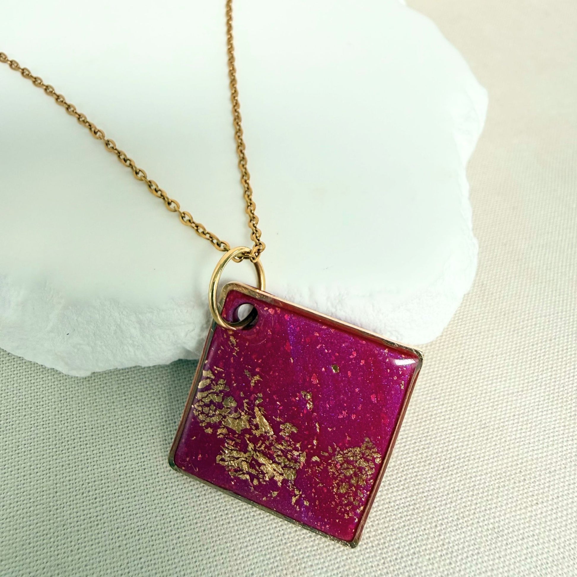 Shine On magenta colour handmade pendant necklace in diamond shape with gold leaf detail and glossy finish hanging from gold toned chain.