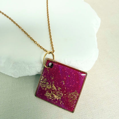 Shine On magenta colour handmade pendant necklace in diamond shape with gold leaf detail and glossy finish hanging from gold toned chain.