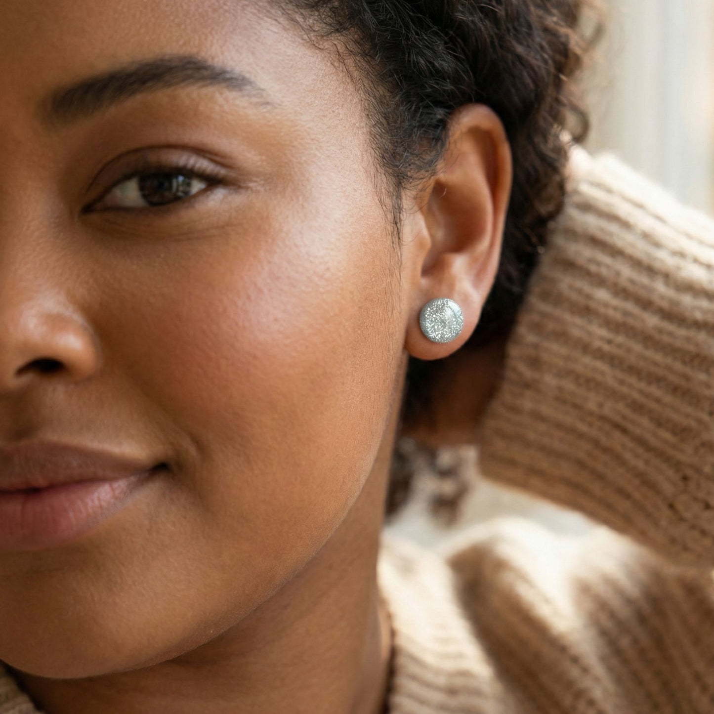 Close-up of a woman wearing silver sparkle stud earrings with a blurred background.