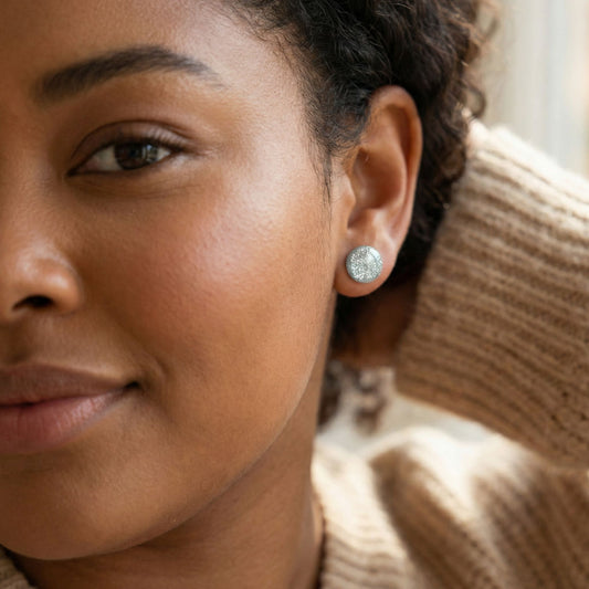 Close-up of a woman wearing silver sparkle stud earrings with a blurred background.