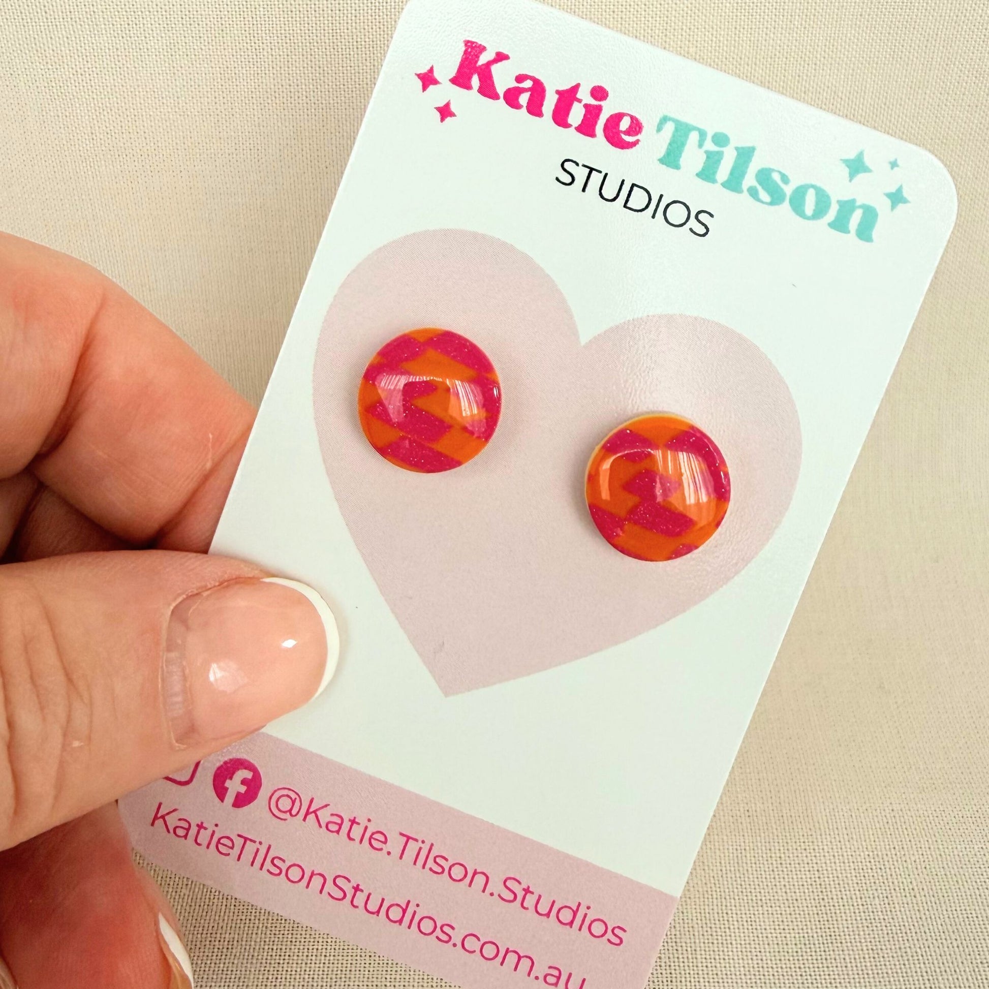 Colorful pink and orange round earrings on a Katie Tilson Studios branded card held by a hand.