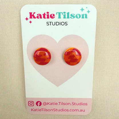 Pink and orange check circular stud earrings on a branded earring card against a beige background.