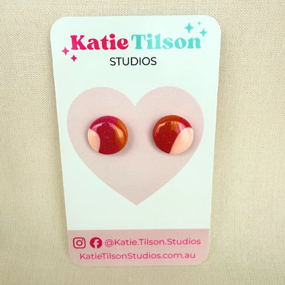 Pair of dark pink, orange and pastel pink colorful stud earrings on a Katie Tilson Studios card against a beige background.