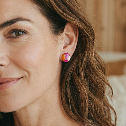 Close-up of a woman wearing colorful pink and orange stud earrings with a blurred background.