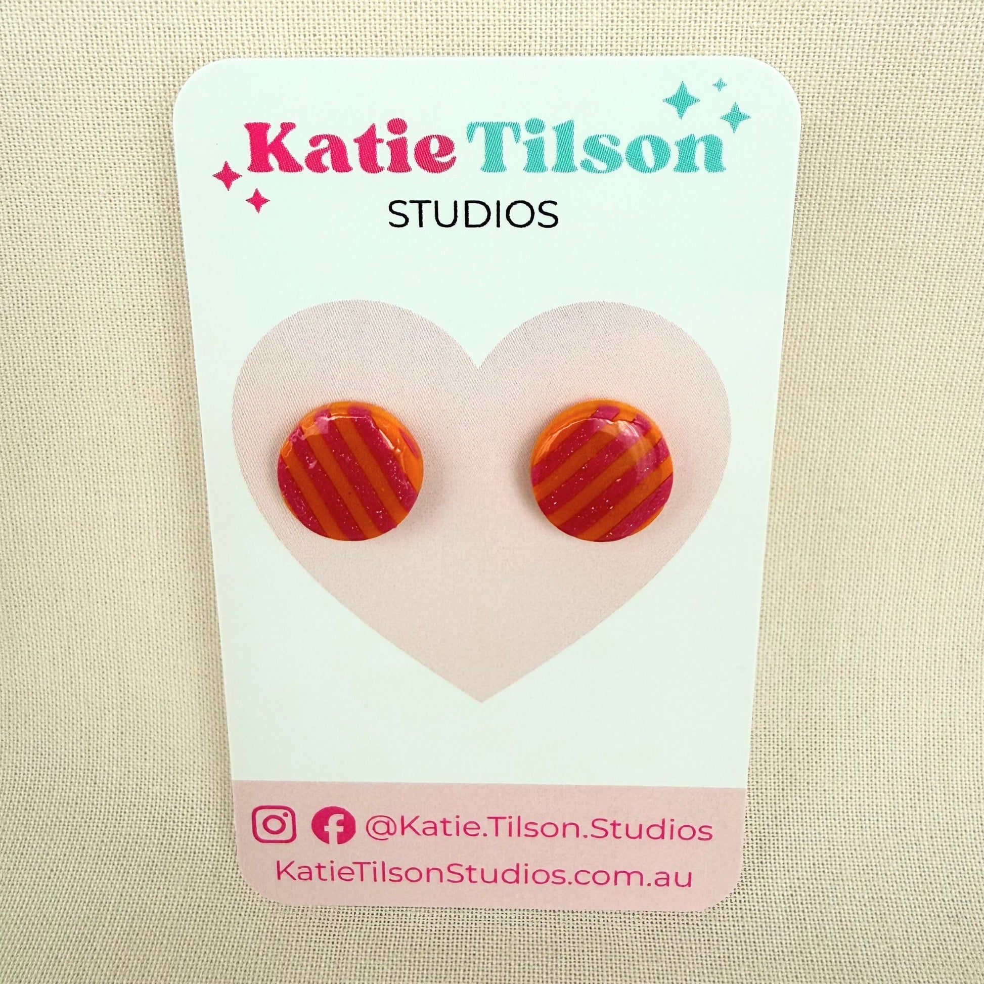 Colorful pink and orange striped circular stud earrings on a Katie Tilson Studios card against a beige background.