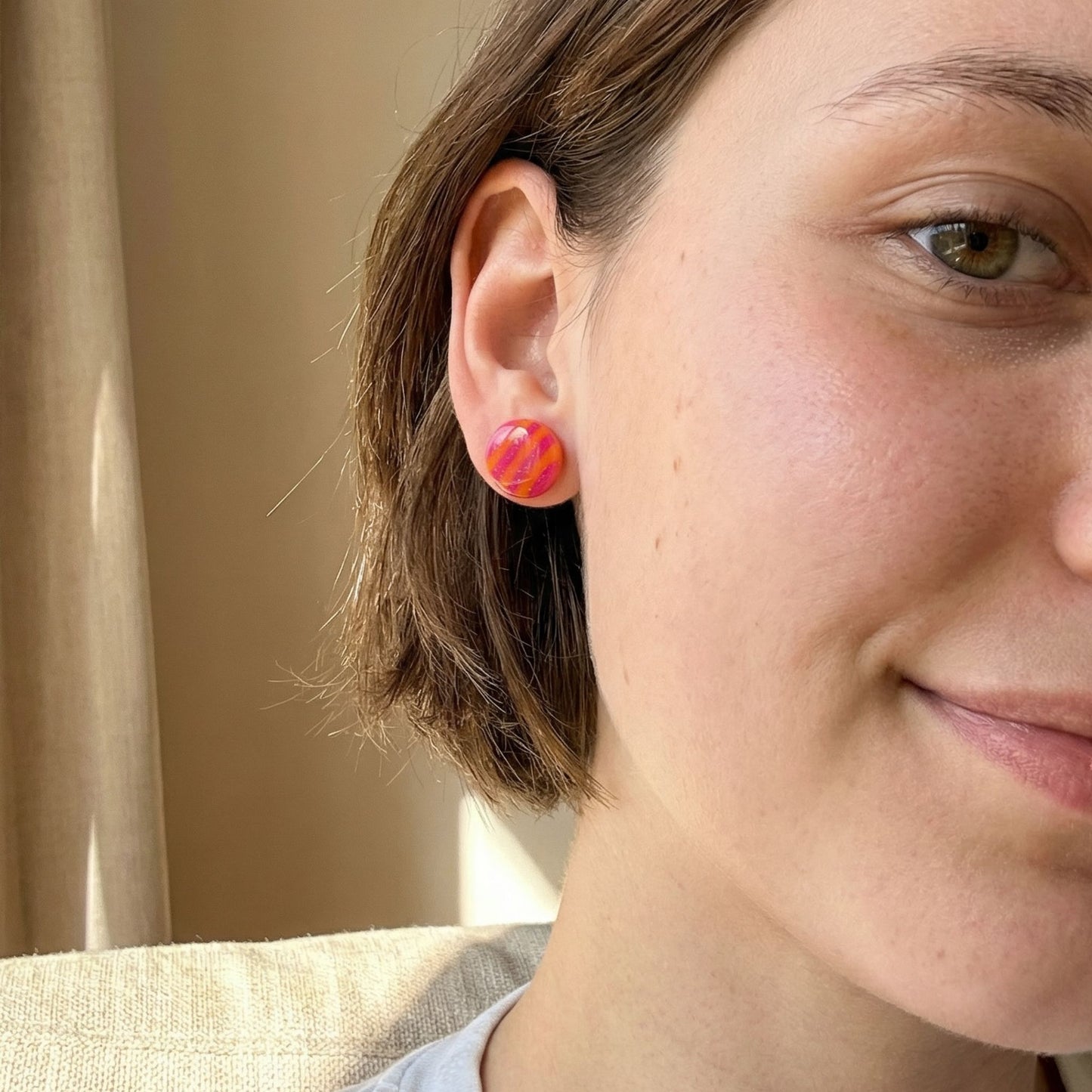 Close-up of a woman wearing pink and orange colorful circular stud earrings with a neutral background.