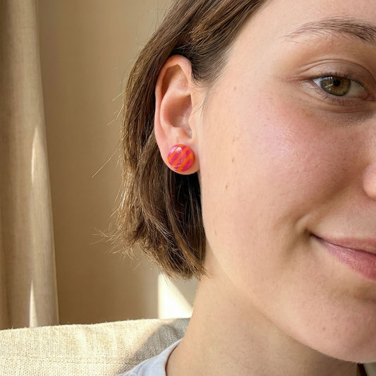 Close-up of a woman wearing pink and orange colorful circular stud earrings with a neutral background.