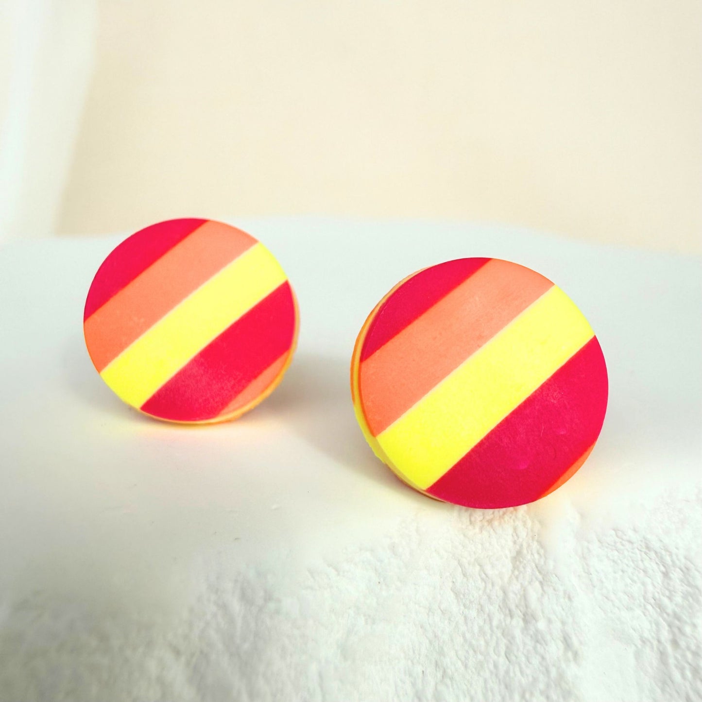 Sunset Pop handmade stud earrings in a red, orange and yellow striped design resting on a white surface.