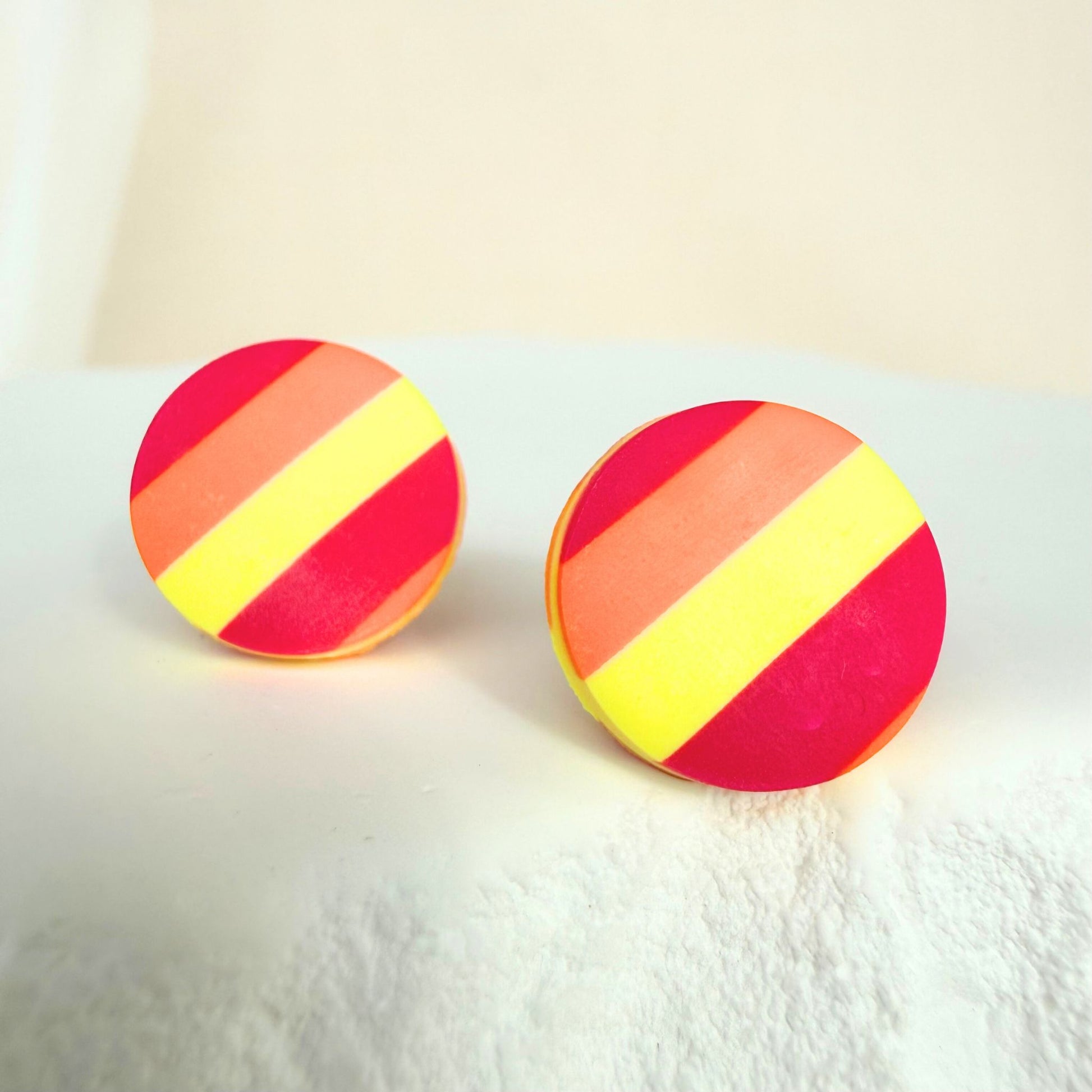Sunset Pop handmade stud earrings in a red, orange and yellow striped design resting on a white surface.