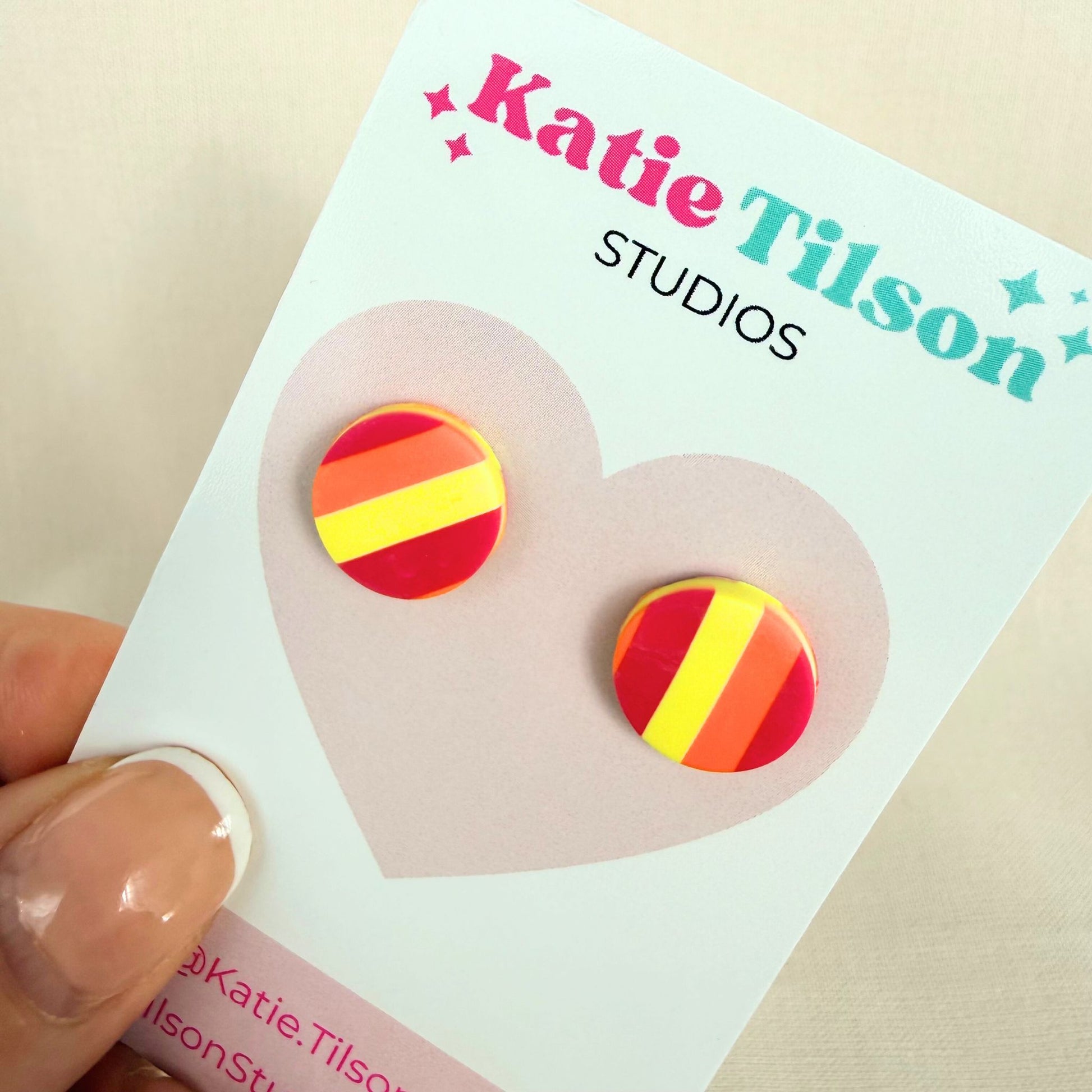 Sunset Pop Australian handmade stud earrings in red, orange and yellow striped design on a Katie Tilson Studios branded earring card held by a hand.