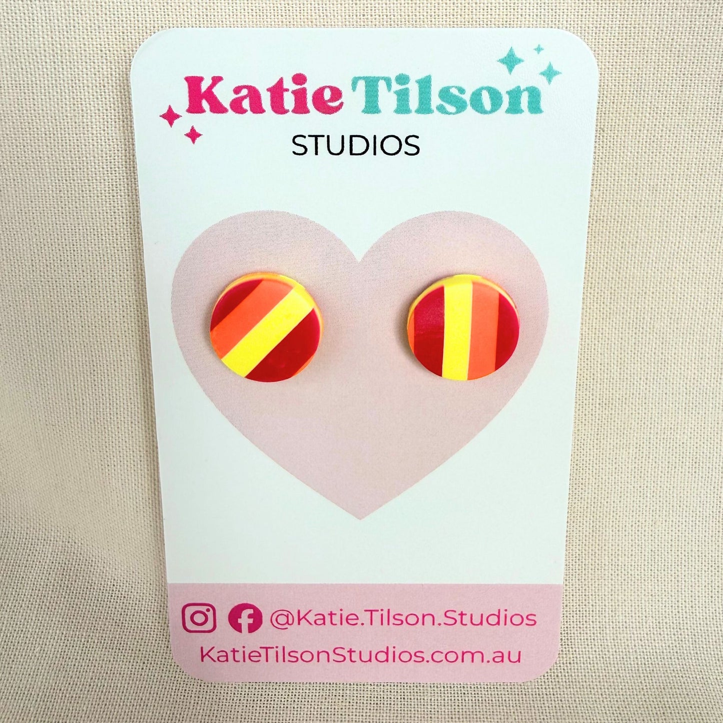 Sunset Pop Australian handmade stud earrings in red, orange and yellow striped design on a Katie Tilson Studios branded earring card against a beige background.