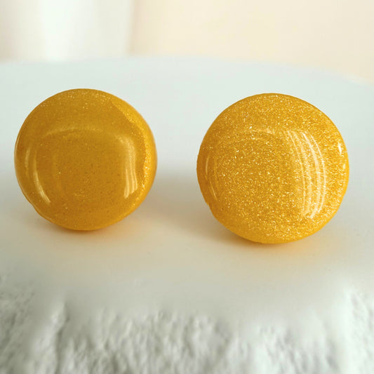 A pair of bright sunshine yellow circle studs with shimmer and glossy resin finish resting on a white surface.