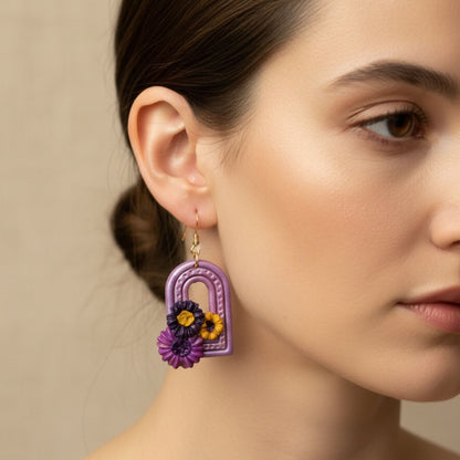 Close-up of a woman wearing Sweet Arch handmade purple floral arch dangle earring against a neutral background.