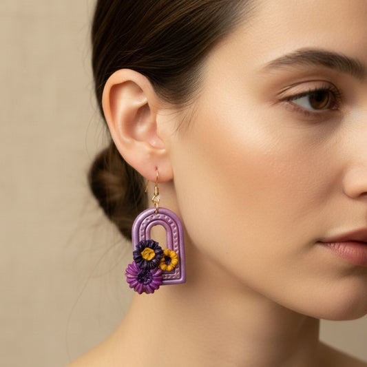 Close-up of a woman wearing Sweet Arch handmade purple floral arch dangle earring against a neutral background.