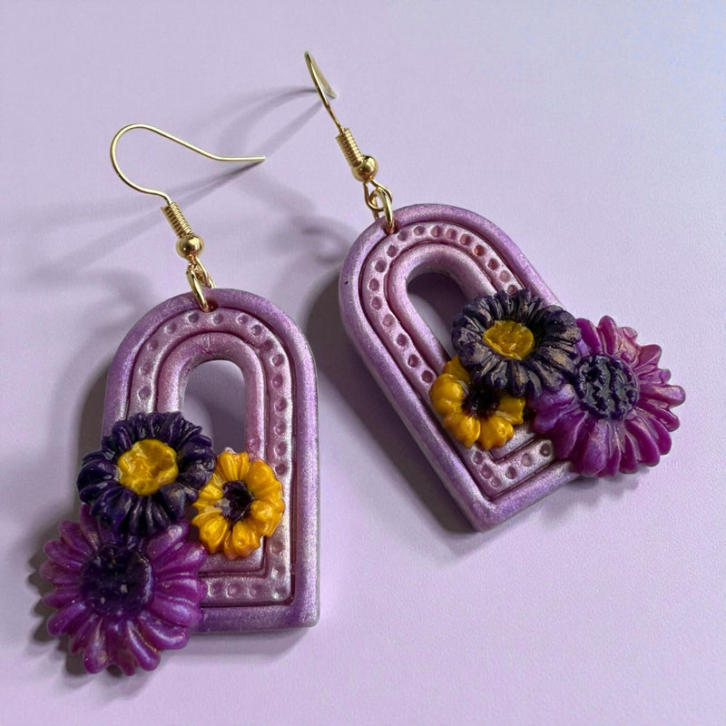Arch-shaped polymer clay earrings with floral designs on a light purple background