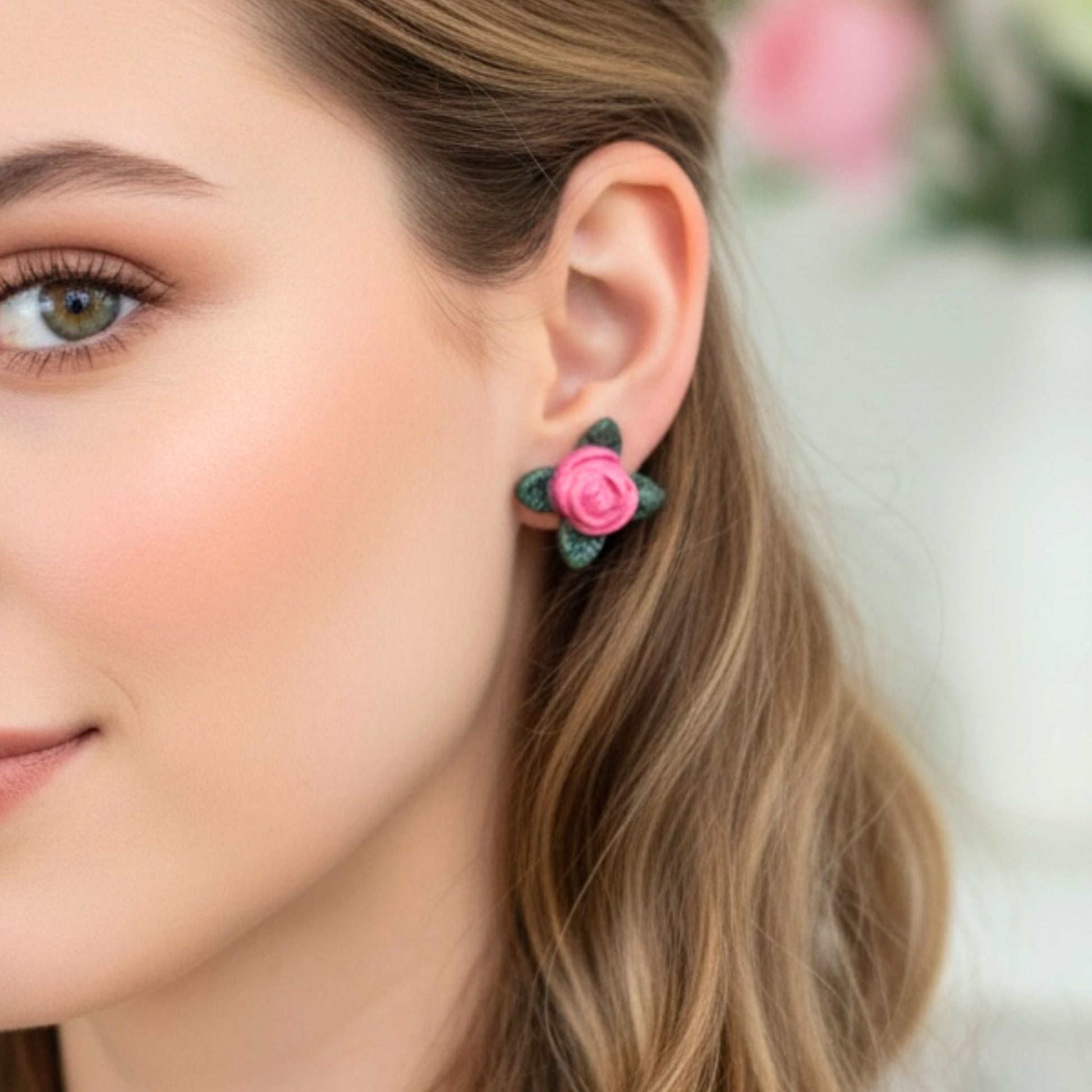 Close-up of a woman wearing pink Sweet Rose stud earrings with a blurred floral background.