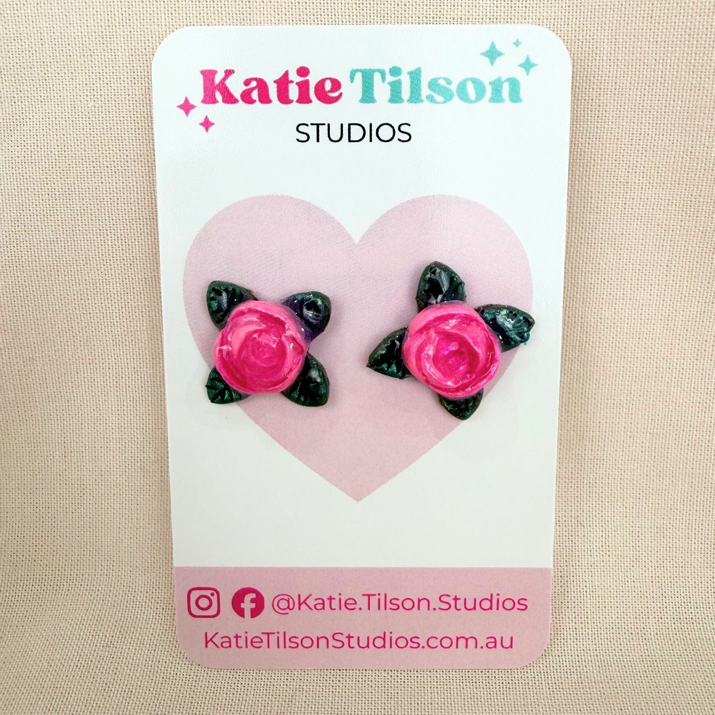 Pink rose stud earrings on a Katie Tilson Studios card against a beige background.
