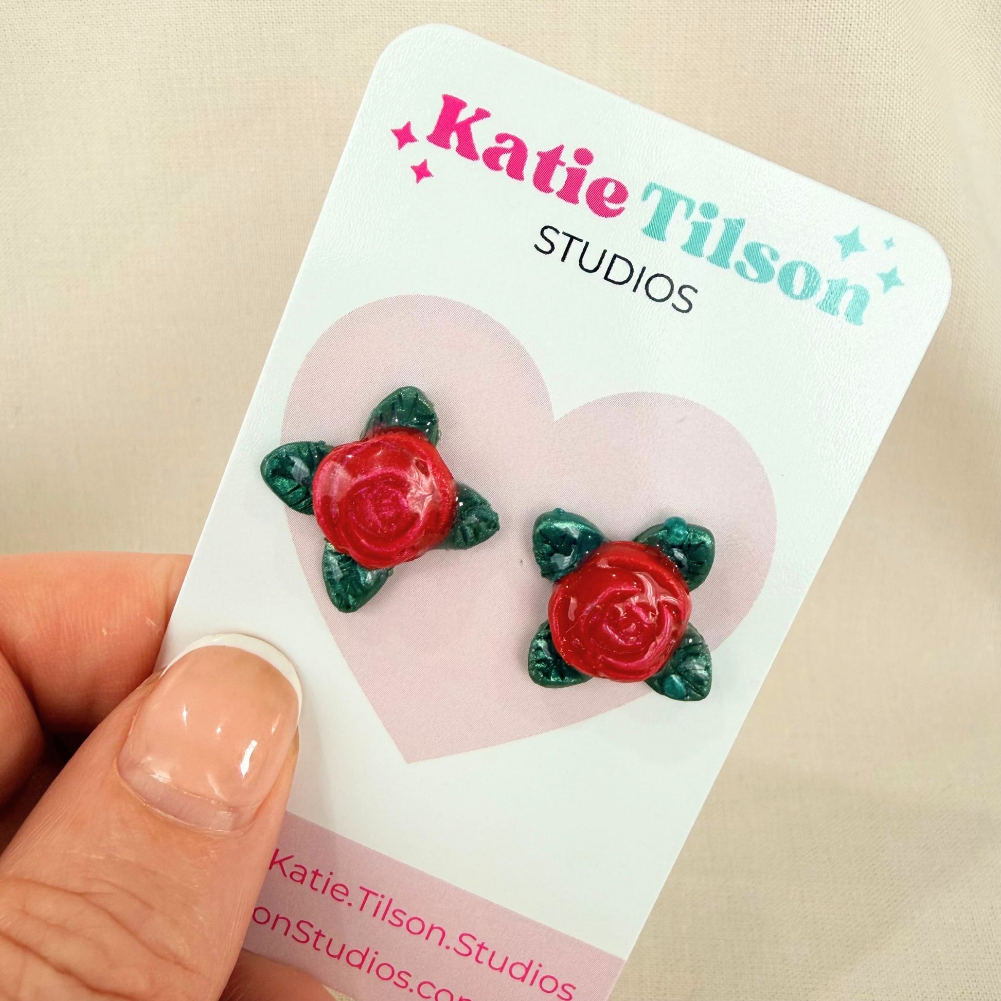 Red rose stud earrings on a Katie Tilson Studios card held by a hand.