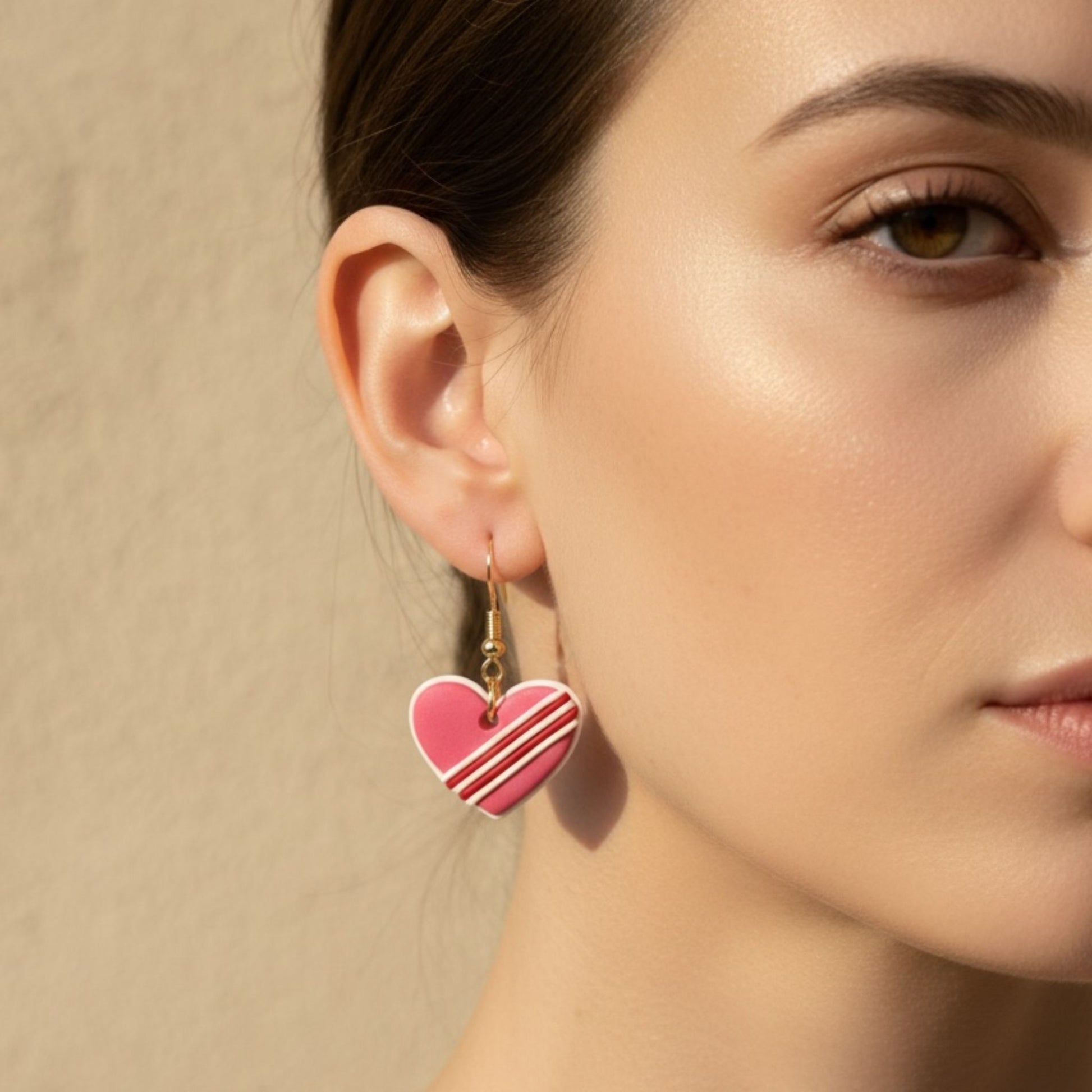 Heart-shaped dangle earrings worn by a model against a neutral background.