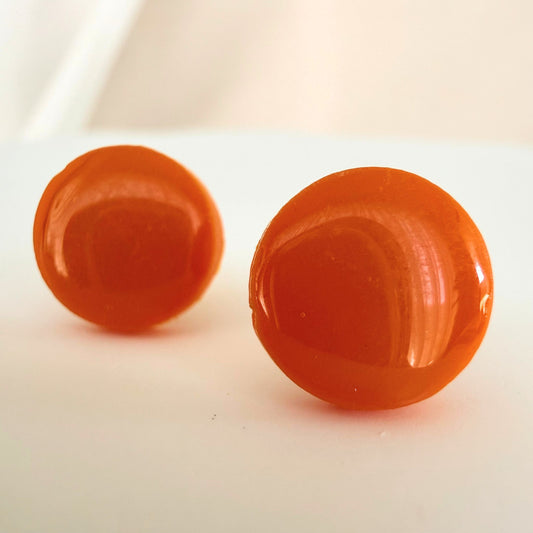 A pair of bright tangerine orange circle studs with a glossy resin finish resting on a white surface.