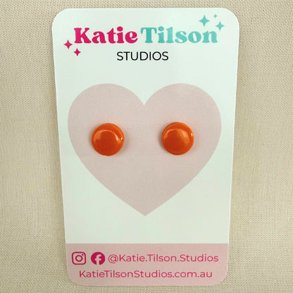 Orange circular stud earrings on a Katie Tilson Studios card.