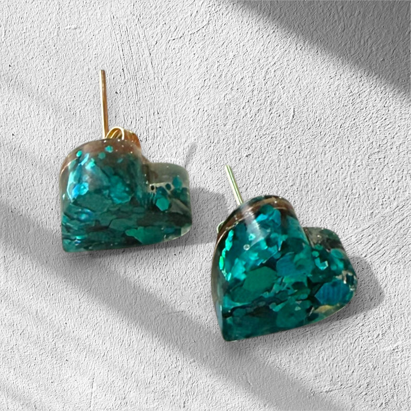 Heart-shaped glitter teal resin earrings on a light gray background