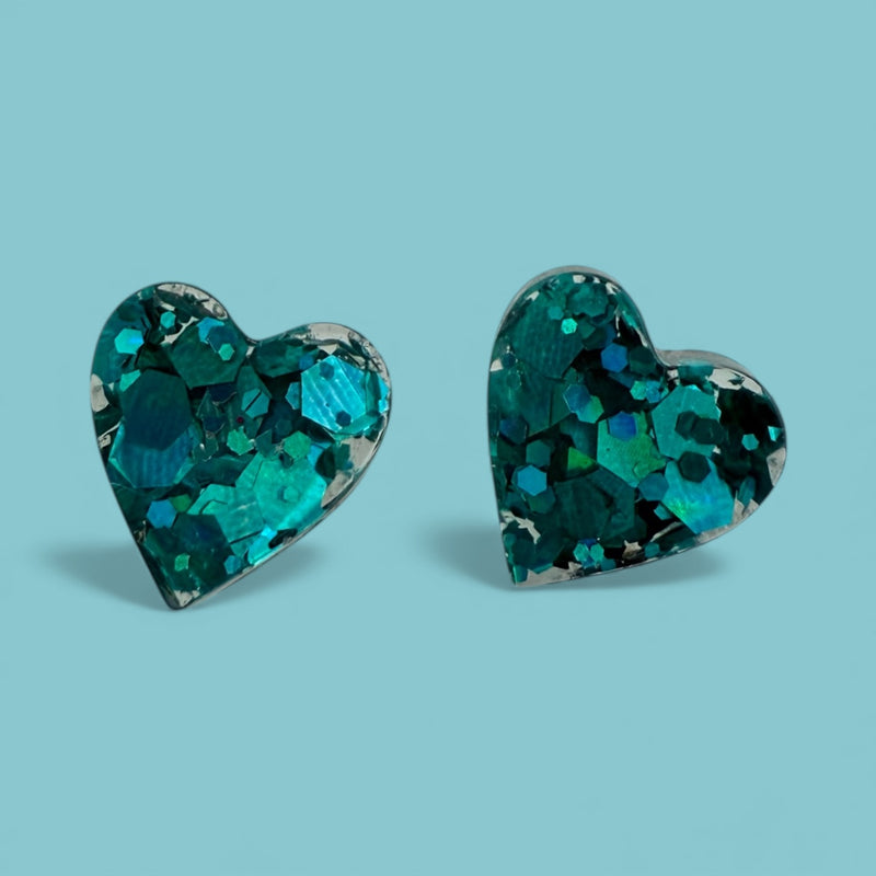 Close-up of teal heart resin stud earrings showing texture on a light blue background.