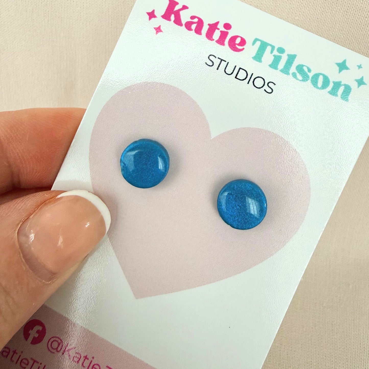 Teal circular stud earrings on a Katie Tilson Studios card held by a hand.