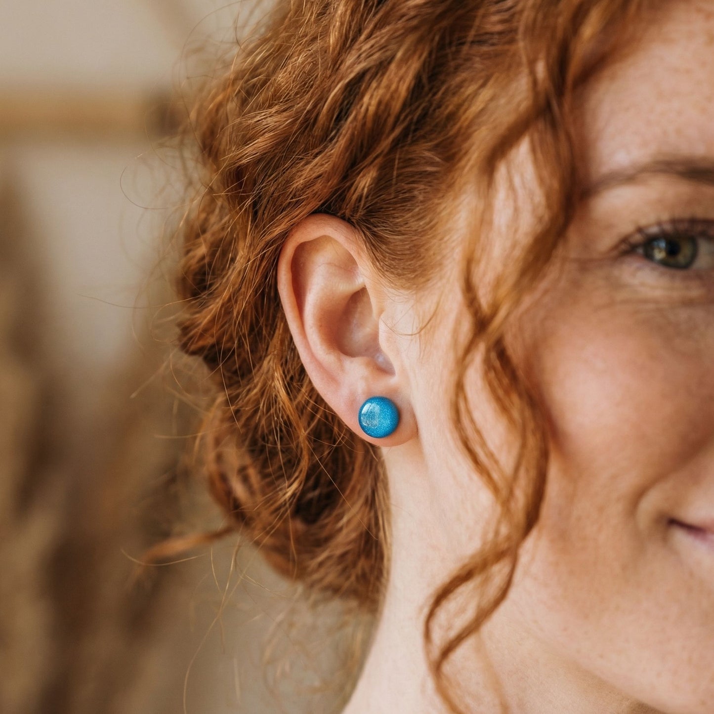 Close-up of a woman wearing teal circular stud earrings with blurred background.