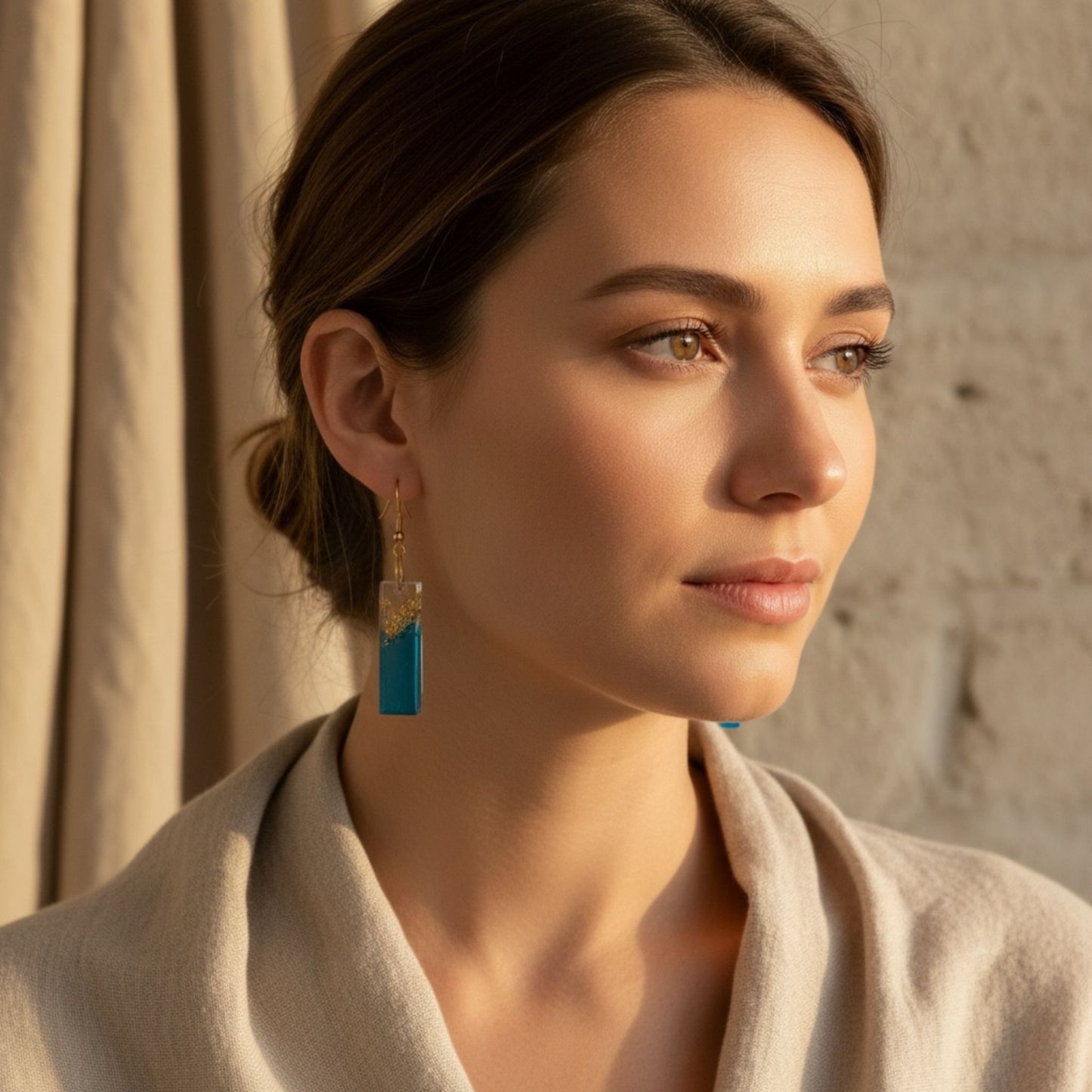 Australian handmade dangle earrings in blue resin with gold leaf detail worn by a woman wearing beige clothing.