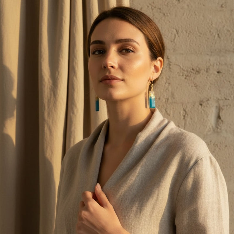 Woman wearing Australian handmade dangle earrings Tidal Bar in blue resin with gold leaf detail.