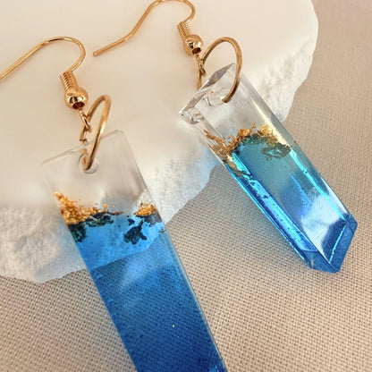 Close up of lightweight handmade dangle earrings Tidal Bar in blue and transparent resin with embedded gold leaf.