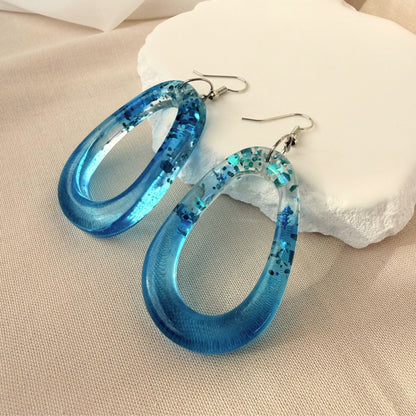 Australian handmade dangle earrings Tidal Glow in translucent teal resin with embedded sparkle.