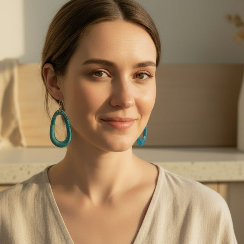 Woman wearing Australian handmade resin dangle earrings in aqua blue hollow oval shape.