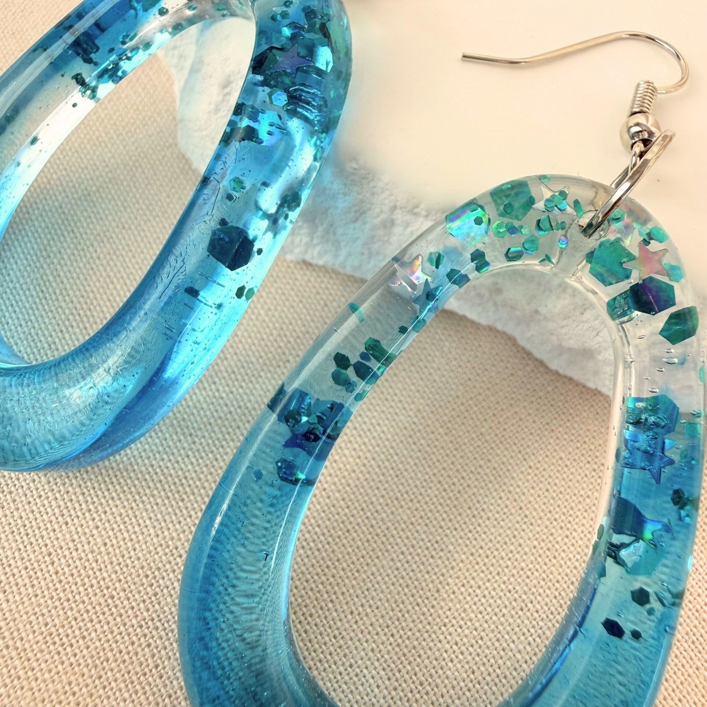 Close up of lightweight handmade dangle earrings Tidal Glow in translucent teal resin with embedded sparkle.