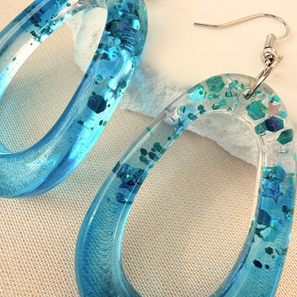 Close up of lightweight handmade dangle earrings Tidal Glow in translucent teal resin with embedded sparkle.