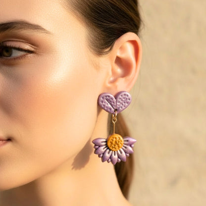 Close-up of a woman wearing purple flower-shaped polymer clay drop earrings with a blurred background.