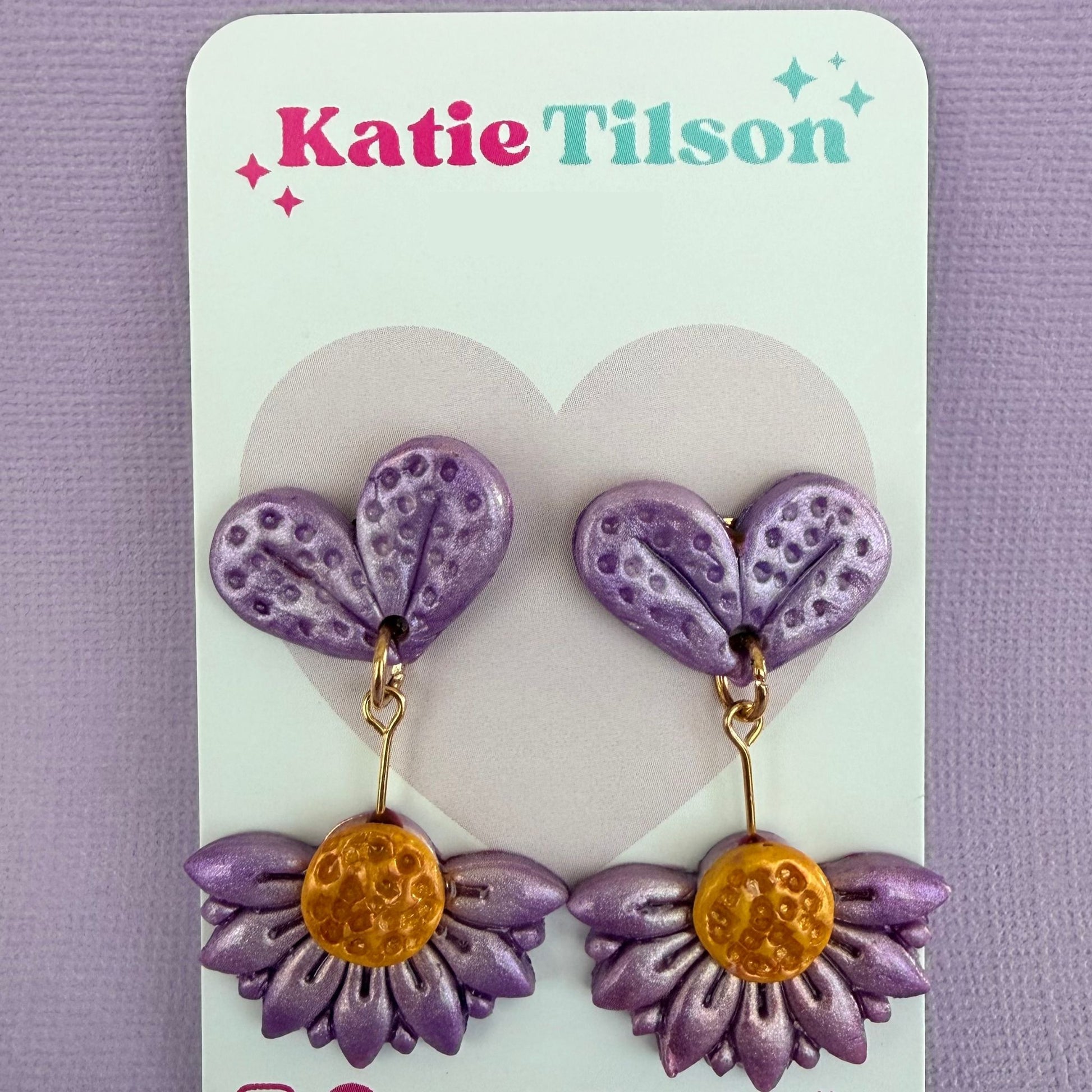 Purple and gold floral drop earrings on a Katie Tilson branded card against a purple background.