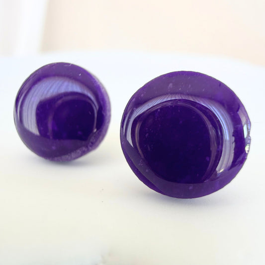 A pair of bright violet purple circle studs with a glossy resin finish resting on a white surface.