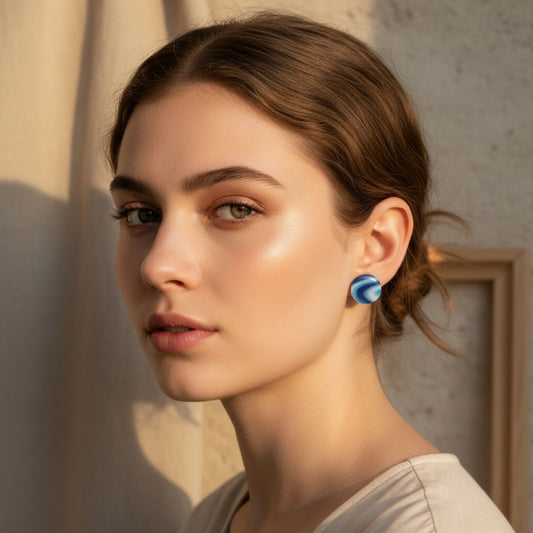 Woman wearing Australian handmade blue round stud earrings with a neutral background behind her.